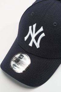 Cappellino da baseball blu navy con logo "NY" ricamato in bianco. Presenta una fascia regolabile e un'etichetta rotonda argento con la scritta "9FORTY."