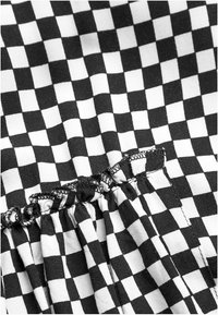 Černo-bílá kostkovaná látka s nařasením podél okraje a viditelným šitím. Textura vypadá hladce a lehce.