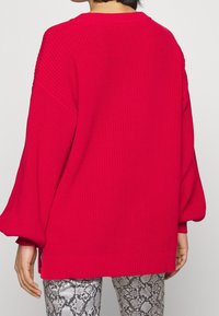 Rød strikket sweater med en løs pasform, ribbede manchetter og kant, der har sænkede skuldre samt et struktureret mønster. Kombineret med bukser i slangeskindsmønster.
