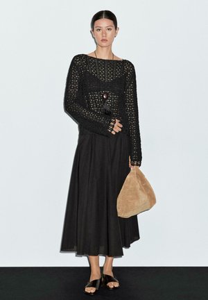 Black knitted sweater with long sleeves, paired with a flowing black skirt, suede bag in beige, and black sandals. Minimalist design.