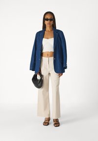 Džínová bunda v tmavomodrej, biela crop top, béžové široké nohavice, čierna kabelka a čierne sandále na remienky; minimalistický, prispôsobený dizajn.