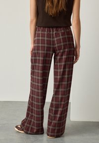 Weit geschnittene Hosen in Burgunderrot und grauem Karomuster, aus weichem Stoff mit elastischem Bund und seitlichen Taschen.