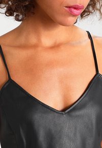 Svart lädercamisole med tunna axelband, med en V-ringning och slät textur, som framhäver plaggets figurnära design.