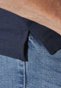 Navy cotton waistband attached to light blue denim, featuring a smooth texture and visible stitching along the edges.