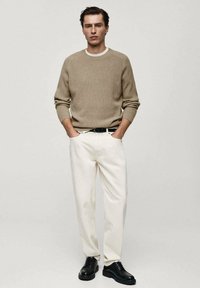 Beige gebreide trui met een ronde hals, witte accenten bij de kraag, gecombineerd met hoge witte broek en zwarte veterschoenen.