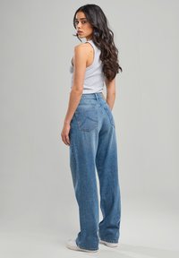 High-waisted blue denim jeans with a relaxed fit, featuring back pockets and a light wash, paired with a gray sleeveless top.