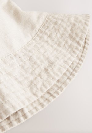 Svetlo bež bombažno blago s prešitim vzorcem, s poševno robom in vidnimi šivi ob podlogi.