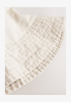 Lichtbeige katoenen stof met een doorgestikte textuur, voorzien van een schuine rand en zichtbare stiksels langs de zoom.