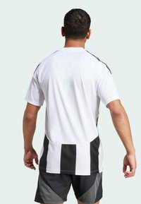 Witte sportieve jersey met zwarte verticale strepen aan de zijkanten, met korte mouwen en een relaxte pasvorm. De textuur lijkt glad en lichtgewicht.