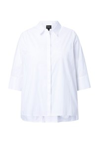 Camicia bianca con colletto, chiusura a bottoni davanti, maniche a tre quarti e orlo posteriore leggermente più lungo. Realizzata in un tessuto liscio.
