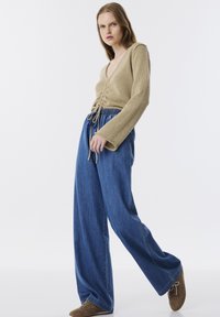Beige gebreide top met een diepe V-hals en centrale knopen, gecombineerd met losse, lichtblauwe denim wijde broekspijpen, met een elastische tailleband.