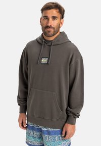 Mørk grå hettegenser med en frontlomme, snor i hetta og en logopatch; paret med mønstrede blå shorts med geometriske design.