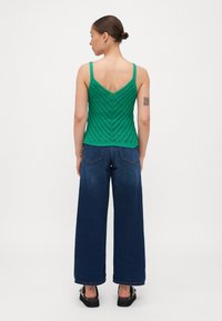 Top de punto verde con un patrón de chevron, combinado con pantalones de mezclilla de pierna ancha en azul oscuro, que presentan un corte holgado y un dobladillo recto.
