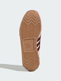 Podrák tenisky Adidas, s vlnitým vzorom trakcie, béžovým gumovým materiálom a logom vyrytým do textúrového povrchu.