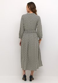 Haljina s crno-bijelim uzorkom, strukirana, dugih naboranih rukava i lepršavom suknjom do gležnjeva. Uparena s crnim potpeticama.