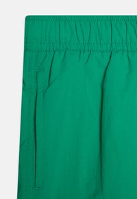 Shorts en tissu vert avec une taille élastique froncée et une poche sur le côté, fabriqués en matériau léger avec une texture douce.