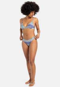 Patterned bikini set featuring a triangular bralette and matching low-rise bottoms in shades of purple and teal with geometric designs.