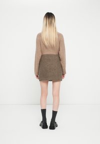 Světle hnědý pletený svetr v kombinaci s sukní s kostkovaným vzorem. Černé robustní boty a tmavě šedé ponožky dotvářejí celý outfit.