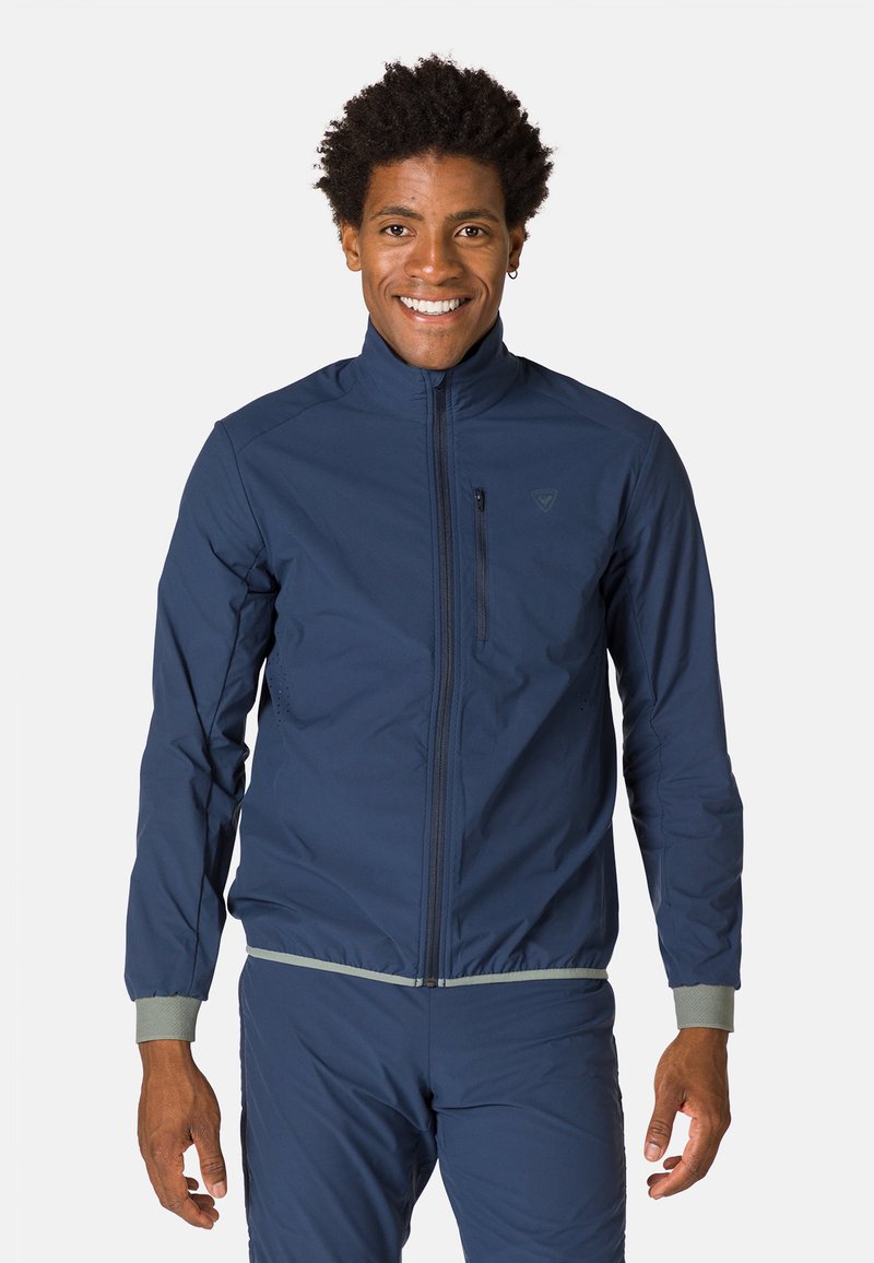 Marineblaue leichte Jacke mit hohem Kragen, Frontreißverschluss und elastischen Bündchen. Verfügt über ein dezent eingesticktes Logo und eine zippertasche auf der Brust.