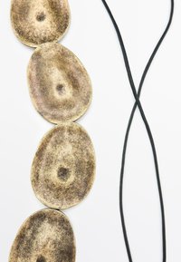 Collana a pendente in ottone con quattro link ovali testurizzati; cordino nero intrecciato. Presenta una finitura metallica invecchiata e bordi arrotondati.