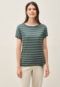 Camiseta a rayas verdes con cuello redondo, mangas cortas con vuelta y un detalle de cordón en la cintura para ajustar. Textura de tela suave.