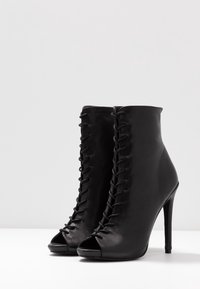 Bottines en cuir noir avec un bout découvert, des lacets à l'avant, un talon aiguille et une texture lisse.