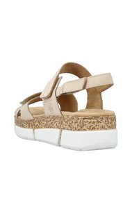 Beige lädersandal med öppen design, kardborreband, strukturerad kork-sula och vit gummisula, som visar upp en modern stil.