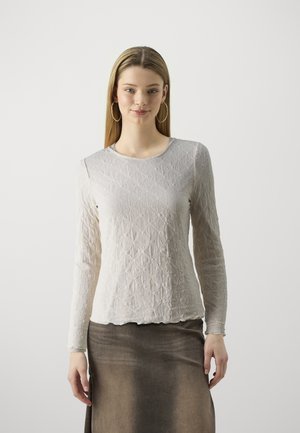 Light gray long-sleeve top with textured diamond pattern, round neckline, and scalloped hem. Paired with a dark brown skirt.