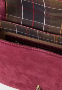 Nyitott bordó velúr kézitáska, amely megmutatja a kockás szövet bélést és a bőr kerettel rendelkező belső cipzáras zsebet.