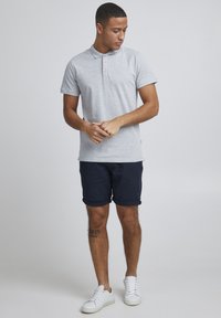 Siva polo majica s ovratnikom i tri gumba, u kombinaciji s tamnoplave kratke hlače. Model ima uski kroj, nosi bijele tenisice. Minimalistički dizajn.