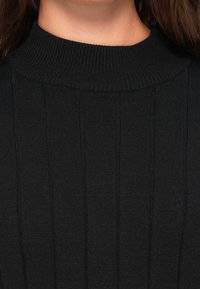 Pull à col roulé en maille côtelée noire, doté d'un col haut et de rayures verticales, fabriqué dans un matériau doux et texturé.