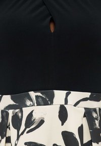 Melnā augšdaļa ar nelielu atslēgas caurumu pie kakla virs baltas svārku ar melnu ziedu rakstu.