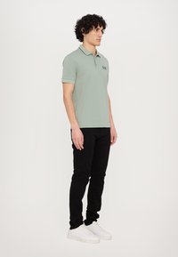 Light green polo shirt with a collar and embroidered logo, paired with black pants and white sneakers. Smooth fabric and tailored fit.