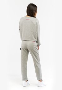 Grau Baumwoll-Sweatshirt und passende Hose, mit rotem Logo auf dem Rücken, lockere Passform, gerippte Bündchen und knöchellange Hosen. Weiße Sneakers.