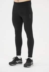 Schwarze sportliche Leggings aus dehnbarem Material, mit einer figurnahen Passform, seitlicher Tasche und einem dezenten Logo entlang des Beins.