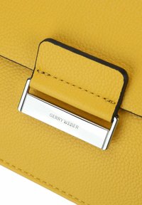 Borsa a mano in pelle gialla con superficie texturizzata, chiusura in metallo argentato con la scritta "GERRY WEBER" incisa e dettagli di cucitura a contrasto.