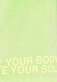 Zelené bavlněné tričko s výrazným žlutým nápisem "MILUJ SVÉ TĚLO" na spodní části. Hladký povrch a design s kulatým výstřihem.