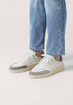 Zapatillas de piel blancas con puntera y talón de gamuza gris. Presentan cordones planos, detalles perforados y una suela gruesa de color crema.