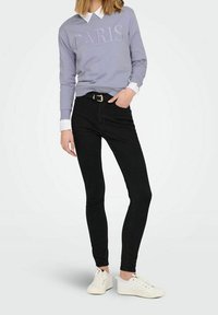 Felpa lilla con la scritta "PARIS", abbinata a jeans skinny neri a vita alta e sneakers bianche. Tessuto morbido, design casual.