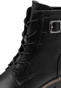 Bottines en cuir noir avec un design à lacets, accent en argent, et surface texturée avec des coutures contrastantes le long des bords.