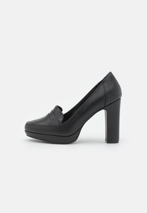 Mocassin noir en cuir à talon haut, bout arrondi, semelle plateforme et talon bloc, présenté en vue latérale sur fond gris.