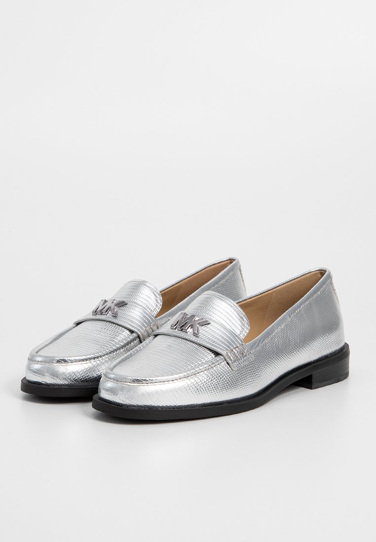 Mocassins métalliques argentés avec une finition texturée, présentant une bande et un détail de logo sur le bout, et un petit talon noir.
