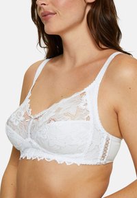 Witte kanten bralette met zachte cups, verstelbare bandjes, bloemige kantdetails en geschulpte randen voor een verfijnde afwerking.