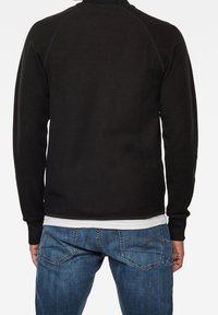 Svart långärmad sweatshirt med ribbat halsringning och manschetter, tillsammans med blå jeans i denim med designade fickor.
