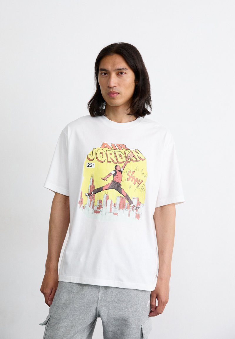 Hvid oversized bomulds T-shirt med et farverigt print af en springende figur sammen med "AIR JORDAN" og en bysilhuet i baggrunden.