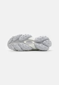 Semelle de sneaker avec un design en caoutchouc texturé en gris clair, dotée de multiples grips arrondis et d'une découpe ovale pour plus de flexibilité.