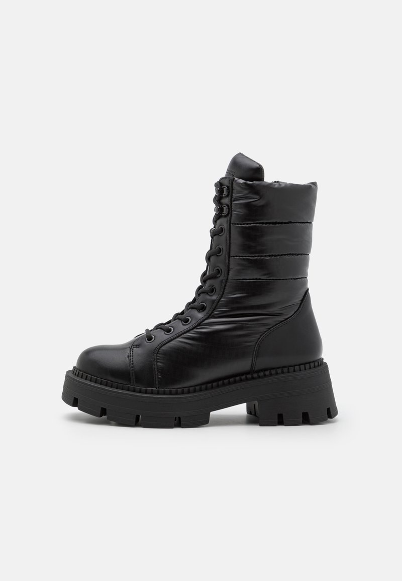Botines negros de tobillo hechos de material sintético suave, con parte superior acolchada, cierre de cordones y una suela gruesa y texturada.