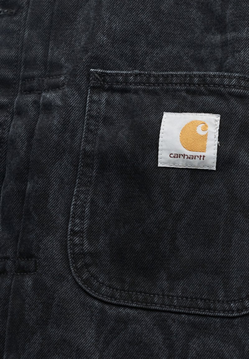 Zwarte denimzak met een wit-gele Carhartt merklabel genaaid vlakbij de rechterbovenhoek.