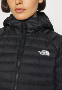 Sort dunjakke med lynlås foran og hætte. Har en quiltet design og det hvide logo fra The North Face på venstre bryst.