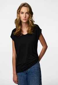 Fekete, rövid ujjú póló kerek nyakkivágással, puha anyagból készült; magas derekú kék farmernadrággal párosítva. Egyszerű és sokoldalú kialakítás.